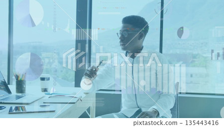 Examining businessman pointing pen toward floating charts in office, with laptop and coffee cup Examining businessman pointing pen toward floating charts in office, with laptop and coffee cup 135443416
