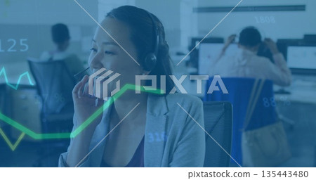Speaking Asian woman in grey blazer handling call at open-plan office, with headset and analytics 135443480