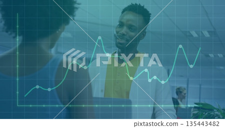 Talking man wearing yellow polo and cardigan in open-plan office, with data graph overlay 135443482
