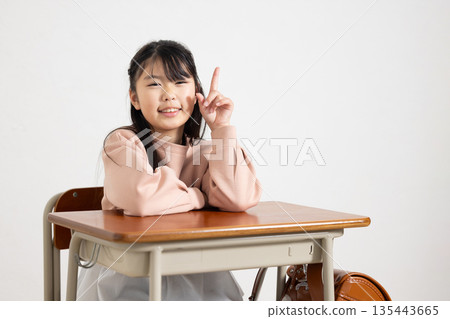 教室裡，一名小學生女孩面帶微笑，豎起食指坐在課桌前。 135443665