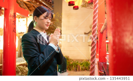 一位身著套裝的年輕女子在夜間於神社祈禱。 135443951