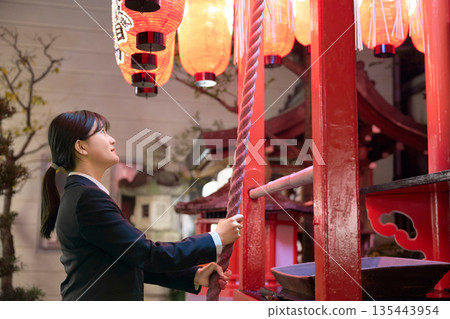 一位身穿西裝的年輕女子在夜晚的神社裡認真地許願。 一位身穿西裝的年輕女子在夜晚的神社裡認真地許願。 135443954
