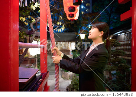 A young woman in a suit making a wish seriously at a shrine at night A young woman in a suit making a wish seriously at a shrine at night 135443958