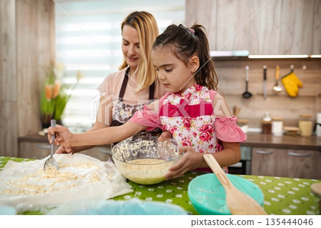 Baking joy shared by mother and daughter in a cozy kitchen Baking joy shared by mother and daughter in a cozy kitchen 135444046
