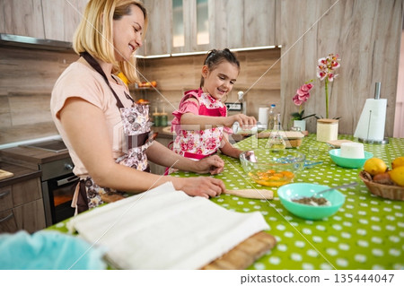 Mother and daughter joyfully baking together in a cozy kitchen Mother and daughter joyfully baking together in a cozy kitchen 135444047
