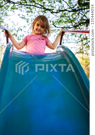 Child enjoying a bright sunny day on a playground slide 135444054