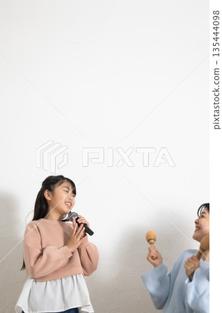 小學生女孩正在享受卡拉OK,她的父母在一旁為她加油。 小學生女孩正在享受卡拉OK,她的父母在一旁為她加油。 135444098