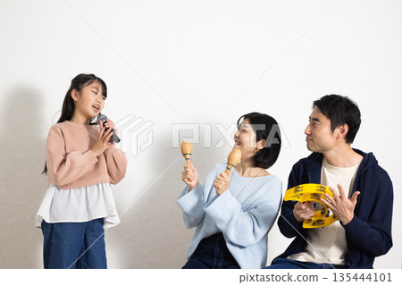 小學生女孩正在享受卡拉OK，她的父母在一旁為她加油。 135444101