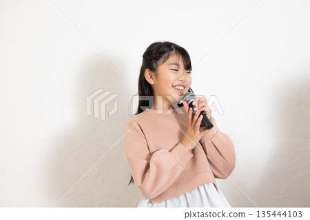 Elementary school girl singing with a microphone Elementary school girl singing with a microphone 135444103