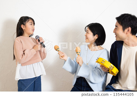 小學生女孩正在享受卡拉OK,她的父母在一旁為她加油。 小學生女孩正在享受卡拉OK,她的父母在一旁為她加油。 135444105