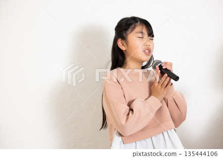 小學生女孩正在享受卡拉OK，她的父母在一旁為她加油。 135444106