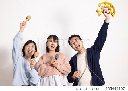 小學生女孩正在享受卡拉OK,她的父母在一旁為她加油。 小學生女孩正在享受卡拉OK,她的父母在一旁為她加油。 135444107