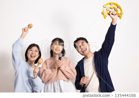 小學生女孩正在享受卡拉OK,她的父母在一旁為她加油。 小學生女孩正在享受卡拉OK,她的父母在一旁為她加油。 135444108