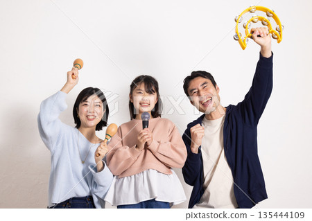 小學生女孩正在享受卡拉OK,她的父母在一旁為她加油。 小學生女孩正在享受卡拉OK,她的父母在一旁為她加油。 135444109