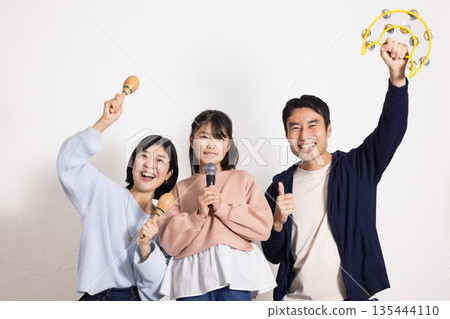 小學生女孩正在享受卡拉OK，她的父母在一旁為她加油。 135444110