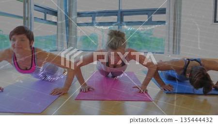 Three women performing push-ups on yoga mats inside fitness studio, with digital overlay 135444432