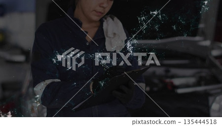 Female automotive technician inspecting engine under open hood at shop, with clipboard and gloves Female automotive technician inspecting engine under open hood at shop, with clipboard and gloves 135444518