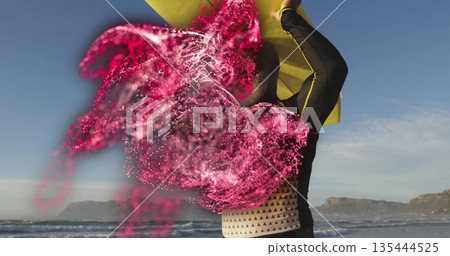 Throwing athletic woman tossing bright magenta powder on sandy beach, with yellow cape billowing Throwing athletic woman tossing bright magenta powder on sandy beach, with yellow cape billowing 135444525
