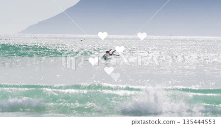Gliding female surfer paddling on surfboard in ocean surf zone, with wetsuit and sparkling waves Gliding female surfer paddling on surfboard in ocean surf zone, with wetsuit and sparkling waves 135444553