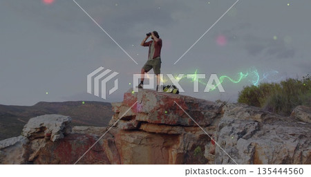 Scanning hiker wearing wide-brimmed hat on cliff with binoculars, backpack and neon trails 135444560