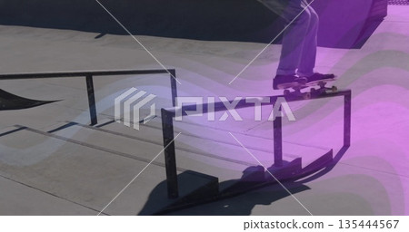 Grinding skateboarder sliding skateboard along metal rail at skate park, with purple overlay Grinding skateboarder sliding skateboard along metal rail at skate park, with purple overlay 135444567