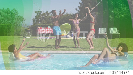 Dancing group of five friends raising arms beside swimming pool in backyard, with inflatable rings 135444575
