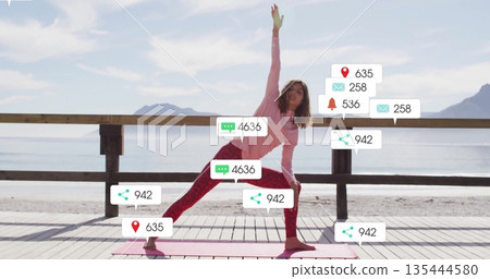 Woman practicing side angle pose on yoga mat on wooden pier by sea with notification icons 135444580