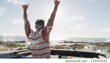 Raising arms mature male celebrating in open-top convertible on coastal path, with social icons 135444581