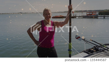 Standing woman in pink top, leggings at dock by lake, holding rowing oar by rowing shell Standing woman in pink top, leggings at dock by lake, holding rowing oar by rowing shell 135444587