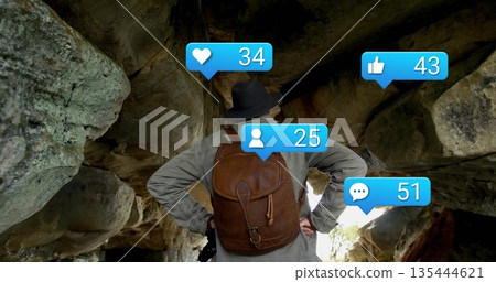 Standing hiker wearing brimmed hat and leather backpack in rock shelter, with social media icons 135444621