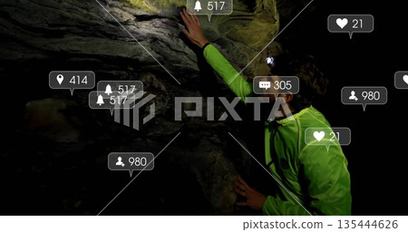 Climbing male explorer gripping cave rock, with headlamp green jacket and social icons, copy space 135444626