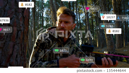 Crouching hunter wearing camo jacket holding crossbow in pine forest, with floating notifications 135444644