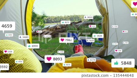 Relaxing camper's red-socked feet extending toward tent opening beside lake, with social icons 135444648