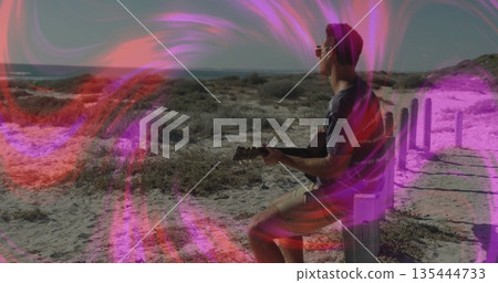 Strumming man wearing sunglasses sitting on post at coastal dunes with acoustic guitar, copy space Strumming man wearing sunglasses sitting on post at coastal dunes with acoustic guitar, copy space 135444733
