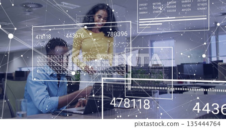 Collaborating technology experts examining network data overlays on laptop in open-plan office 135444764