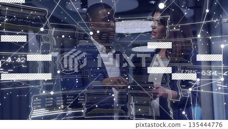 Two professionals wearing suits reviewing holographic data panels with tablet in server room Two professionals wearing suits reviewing holographic data panels with tablet in server room 135444776