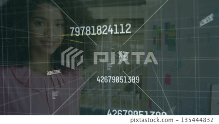 Standing female professional interpreting data overlay in office workspace, sticky notes and charts 135444832