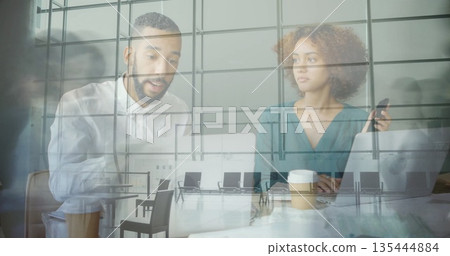 Two professionals collaborating at conference table, with laptops and grid reflection on glass wall Two professionals collaborating at conference table, with laptops and grid reflection on glass wall 135444884