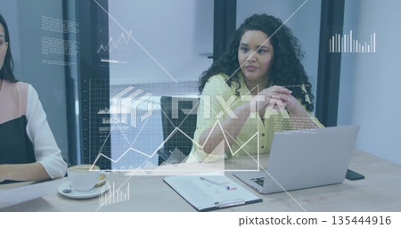 Analyzing floating data charts woman in yellow blouse typing on silver laptop in conference room 135444916