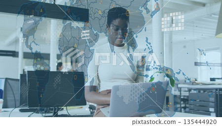 Working data analyst typing on silver laptop in open-plan office, with digital world map overlay Working data analyst typing on silver laptop in open-plan office, with digital world map overlay 135444920