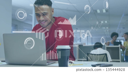Leaning man wearing red sweater working on laptop at open-plan office with data visualizations 135444928
