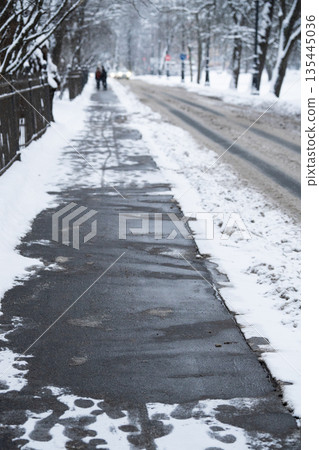 Snowy city road coated with chemicals and technical salt against ice formation in winter season. 135445036