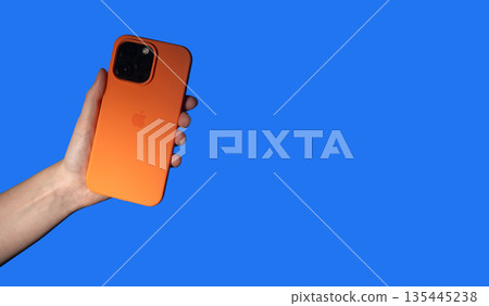 Lodz Poland May 25 2025 Hand holding smart phone. Modern mobile device in bright orange protection Lodz Poland May 25 2025 Hand holding smart phone. Modern mobile device in bright orange protection 135445238