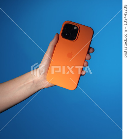 Lodz Poland May 25 2025 Hand holding smartphone. Modern mobile device in bright orange protective 135445239