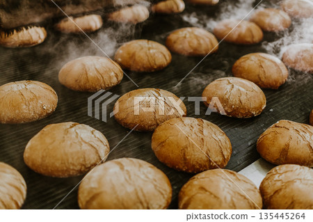 Fresh buns from the oven. Conveyor with bread. Baking bread. Workshop for production of bread. White bread in the oven. Hot buns. Confectionery 135445264