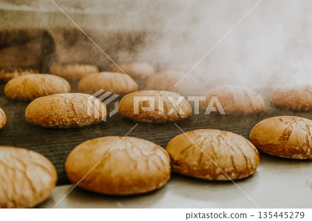 Fresh buns from the oven. Conveyor with bread. Baking bread. Workshop for production of bread. White bread in the oven. Hot buns. Confectionery 135445279