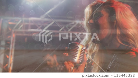 Singing woman wearing leather jacket, holding vintage microphone on stage with colored spotlights Singing woman wearing leather jacket, holding vintage microphone on stage with colored spotlights 135445358