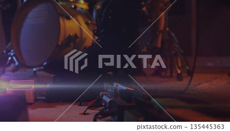 Pressing musician's leather boot activating guitar pedals on stage, with bass drum and audio cables 135445363
