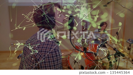 Singing vocalist wearing headphones into mic in studio with drummer at drum kit, copy space Singing vocalist wearing headphones into mic in studio with drummer at drum kit, copy space 135445364