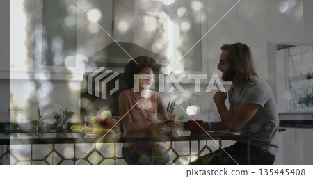 Chatting couple sipping coffee and checking smartphone at kitchen island, with red mugs, fruit bowl 135445408